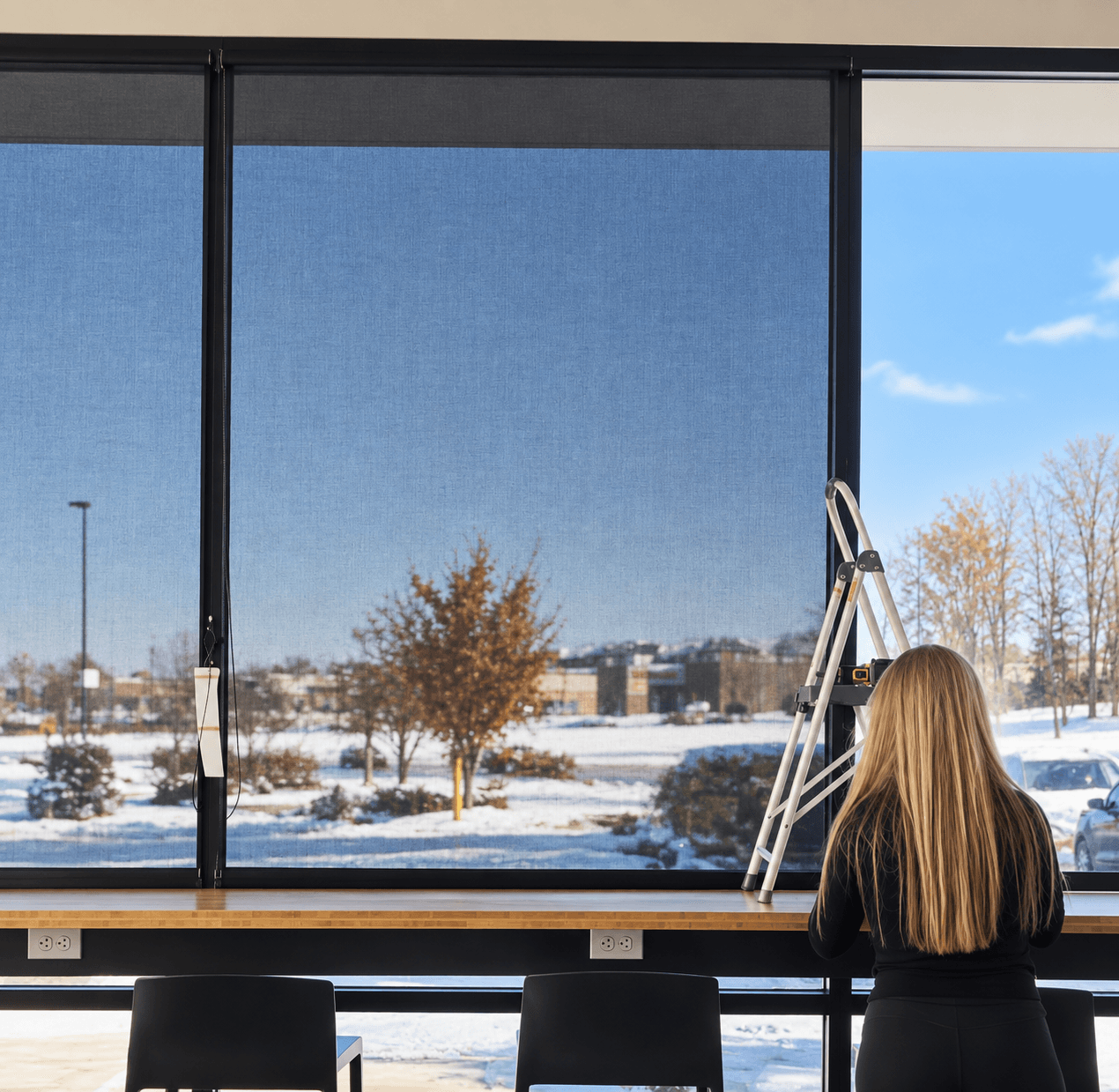 Installer completing a set of dark solar shades across wide commercial windows